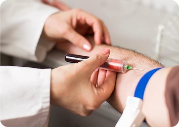 Close-up view of a healthcare worker drawing blood into a syringe from a patient’s arm secured with a blue tourniquet.