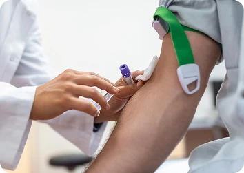Close-up of a medical professional collecting a blood sample from a patient’s arm secured with a green tourniquet.