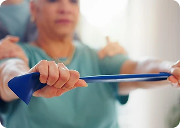 Older woman performing a resistance-band stretch with a blue band under a therapist’s guidance.
