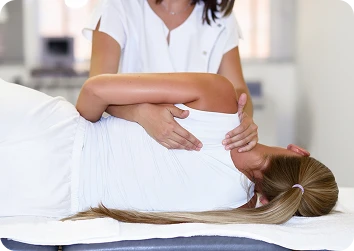 Female patient lying on her side on a treatment table while a therapist supports her shoulder and neck during a spinal adjustment.