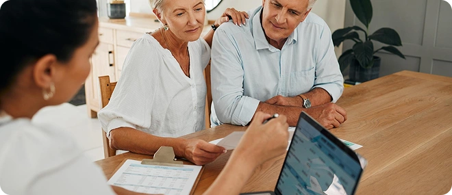 Elderly couple reviewing documents with a consultant taking notes at a table during a meeting