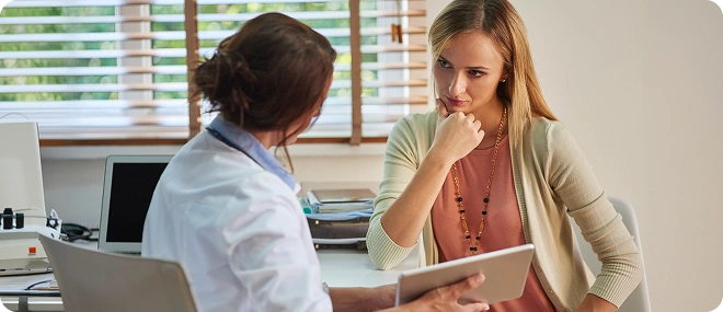 Doctor showing a tablet to a thoughtful female patient during a consultation at a desk