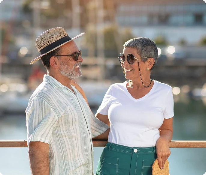 Smiling mature couple in sunglasses standing together at a sunny marina.