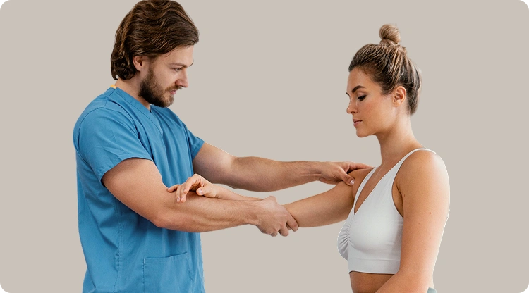 Physical therapist in blue scrubs performing an arm and shoulder mobility assessment on a female patient against a neutral background