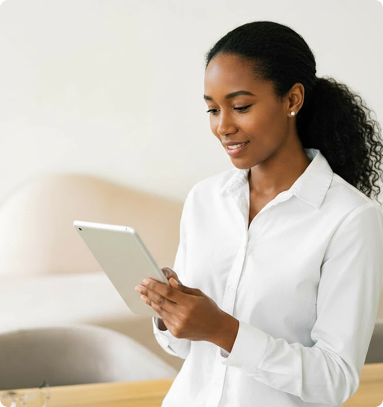 Smiling young woman in a white button-down shirt using a tablet in a bright, minimal interior.
