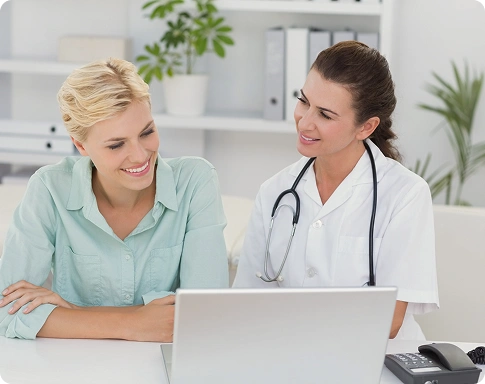 Female doctor with a stethoscope and a smiling female patient looking at a laptop together during a consultation
